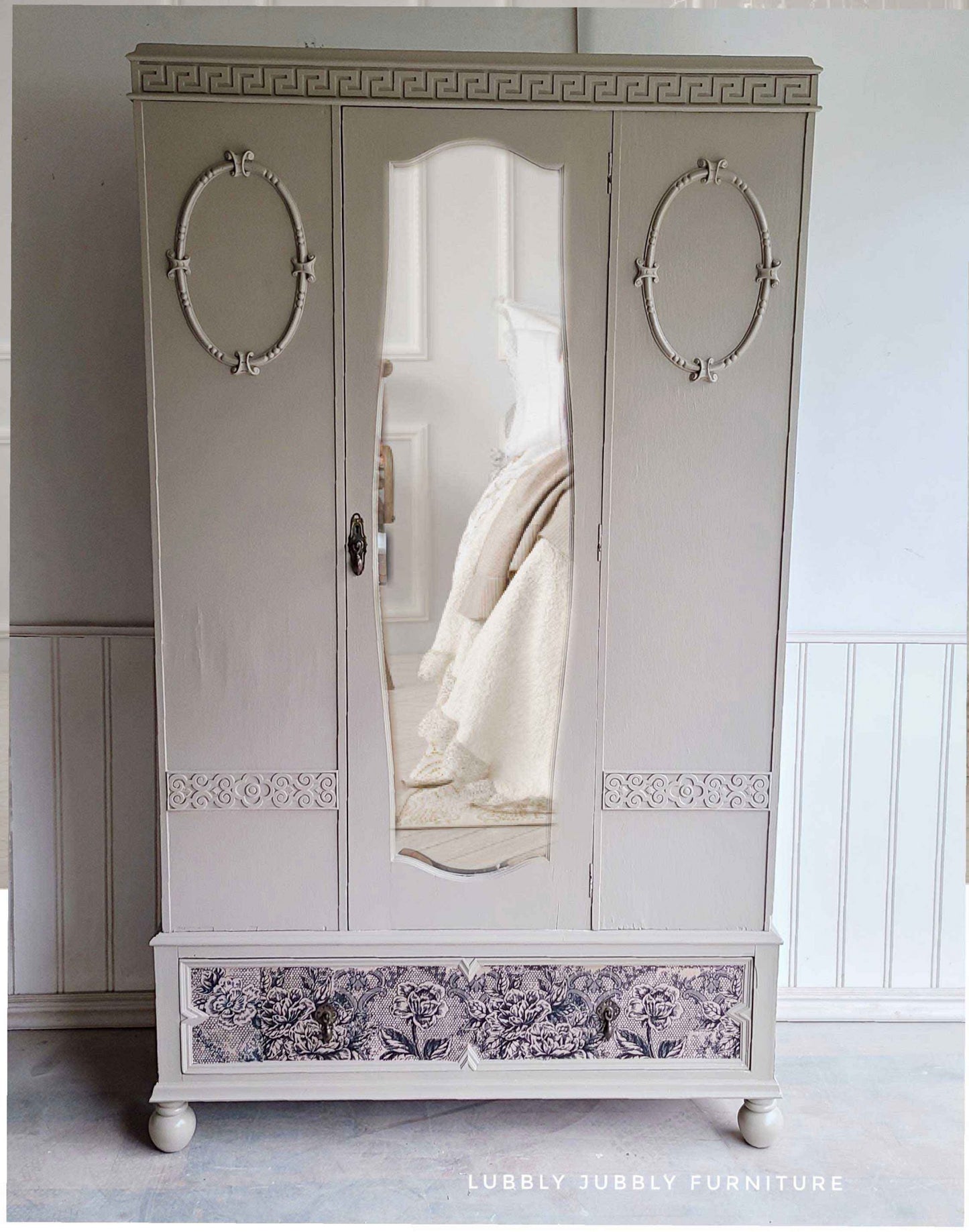 Tall vintage wardrobe painted in a soft neutral tone with Antique Laces decoupage fiber paper decorating the bottom drawer.