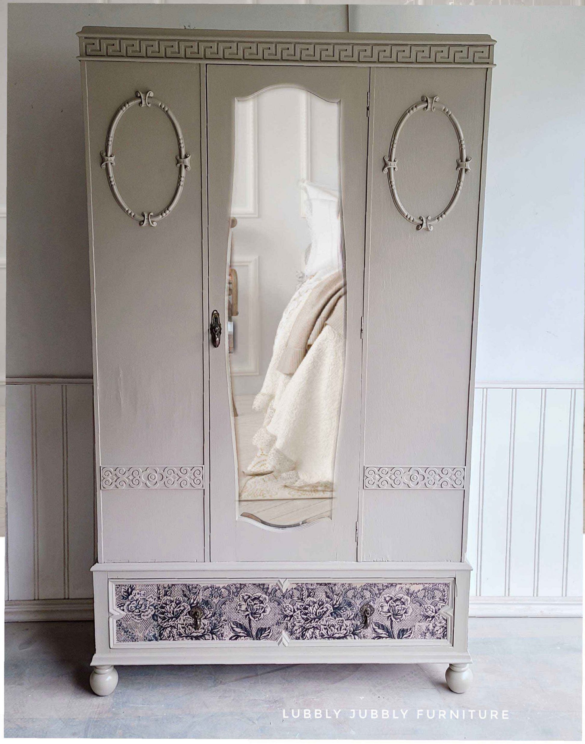 Tall vintage wardrobe painted in a soft neutral tone with Antique Laces decoupage fiber paper decorating the bottom drawer.