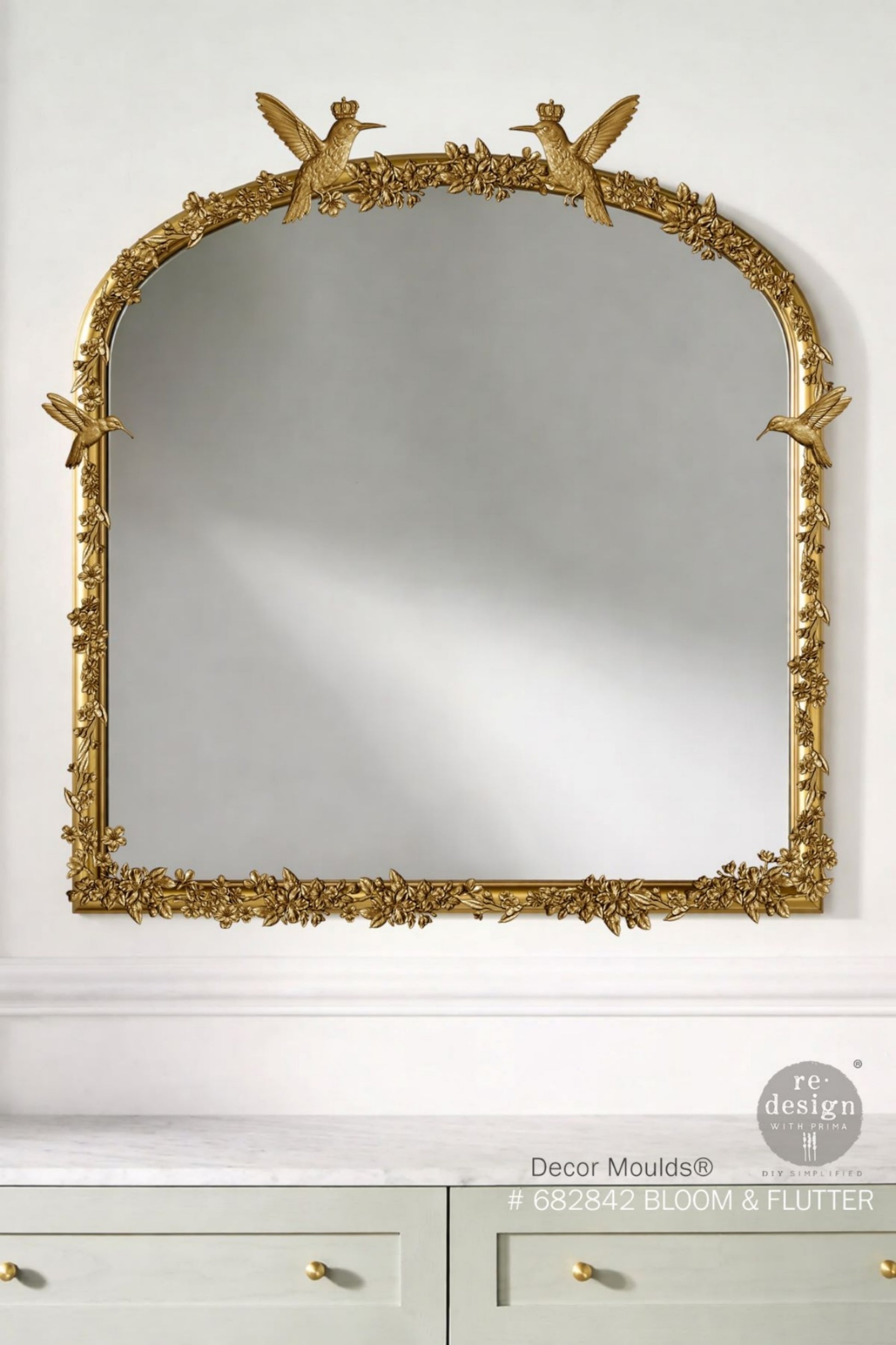 Garden-inspired Bloom & Flutter silicone mould featuring flying hummingbirds, soft flowers, leafy branches, and decorative crown embellishments shown on a gold mirror close up