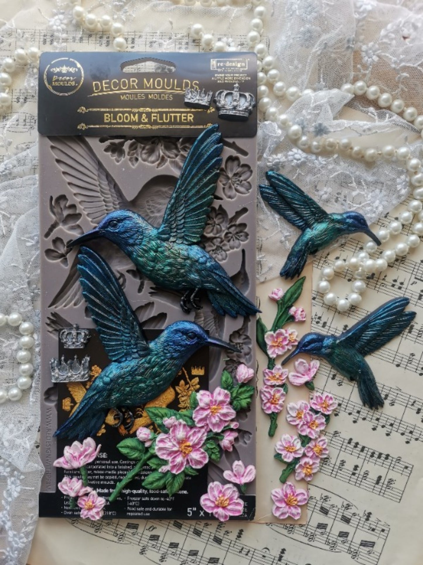 Painted castings made from the Bloom & Flutter mould featuring turquoise hummingbirds, pink blossoms, branches, leaves, and crowns.
