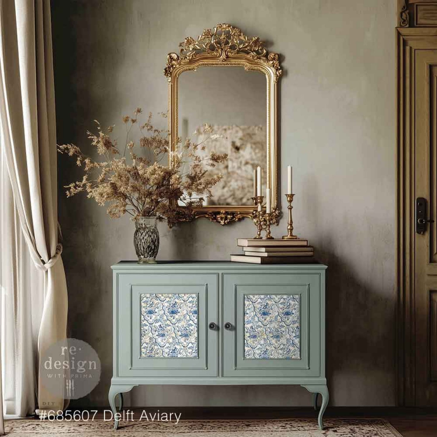 Delft Aviary decoupage fiber applied to the inset cabinet doors of a soft blue-green vintage cabinet, styled with a gold ornate mirror, brass candlesticks, books, and dried florals.