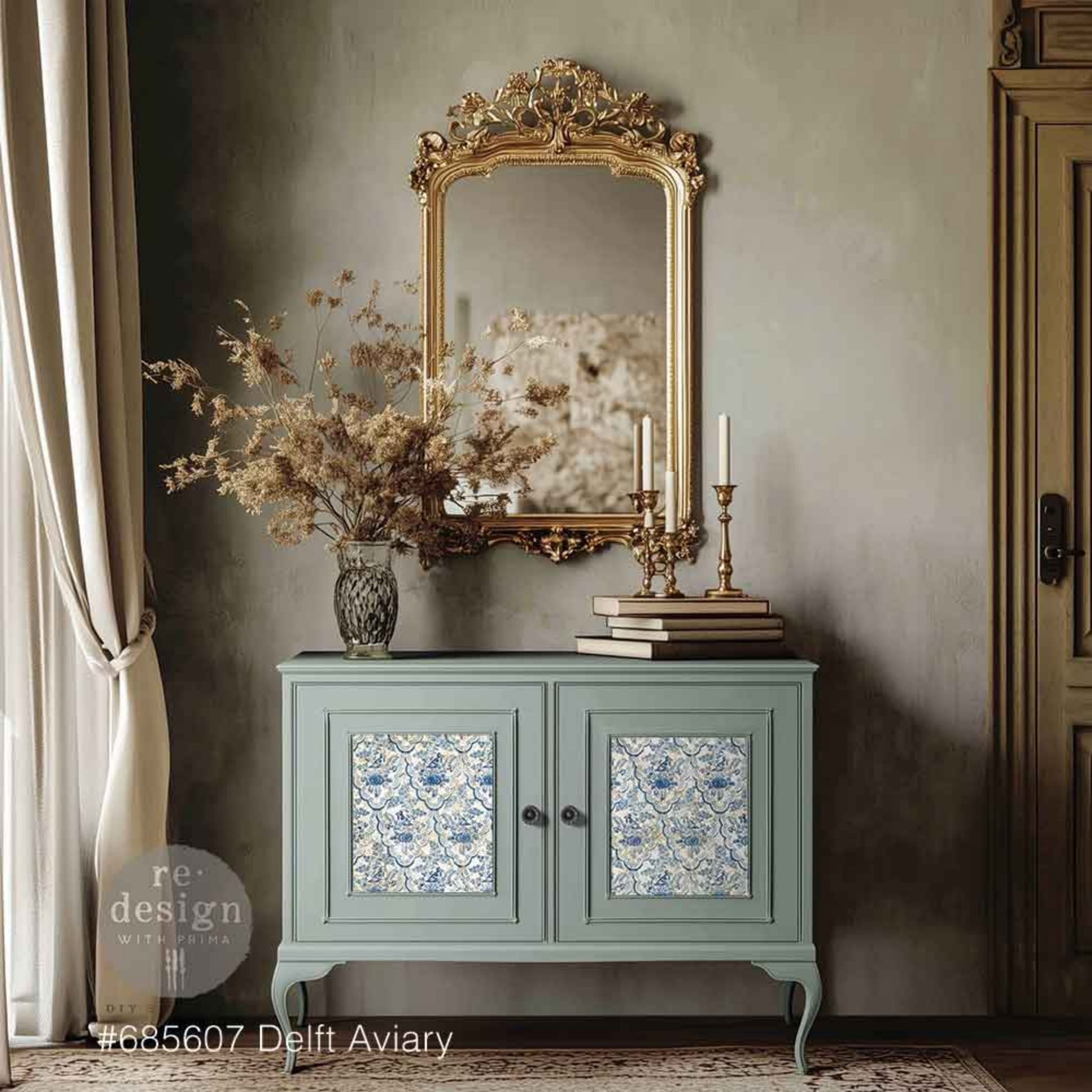 Delft Aviary decoupage fiber applied to the inset cabinet doors of a soft blue-green vintage cabinet, styled with a gold ornate mirror, brass candlesticks, books, and dried florals.