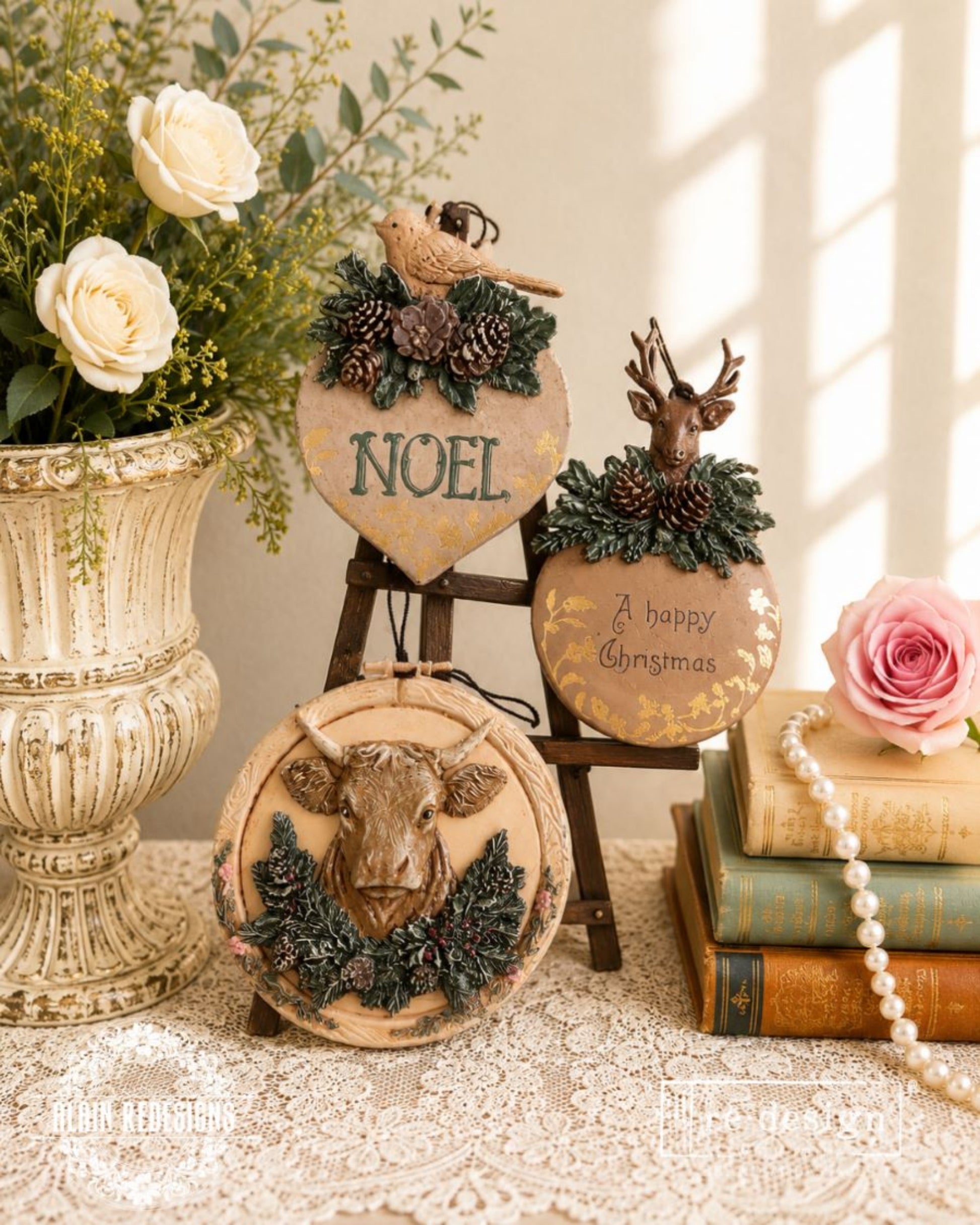 Three finished holiday plaques featuring a bird, deer, and cow with evergreen and pinecone embellishments.