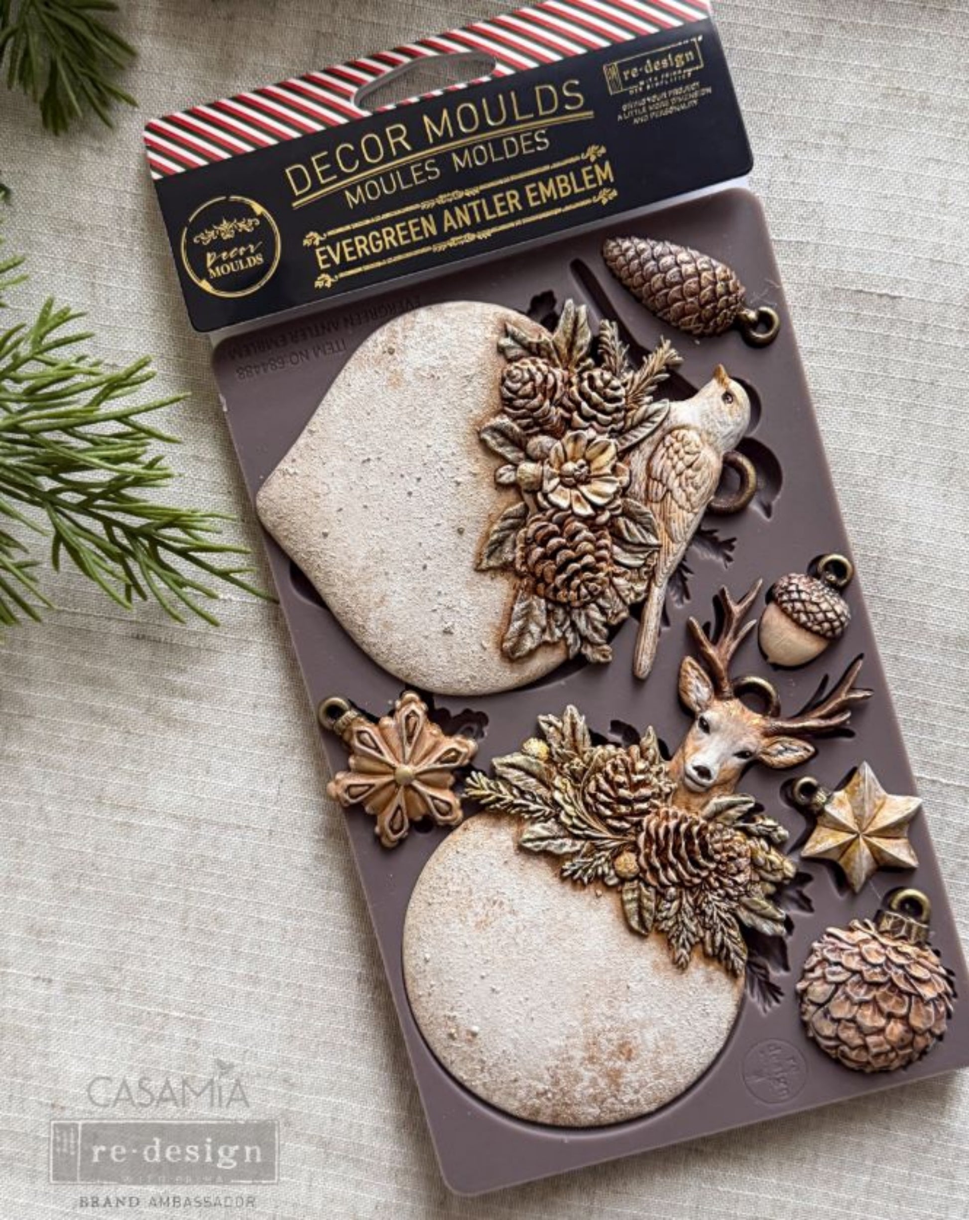 Packaged Evergreen Antler Emblem Décor Mould with painted bird, deer, pinecone, acorn, star, and snowflake castings.
