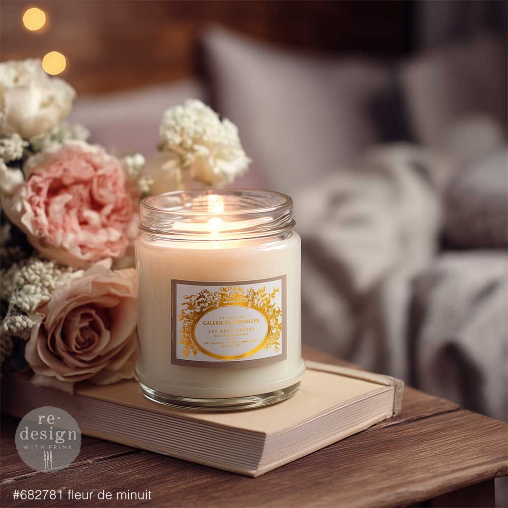 Fleur De Minuit gold H2O transfer label applied to a glass candle jar styled with soft flowers, book, and cozy home décor.