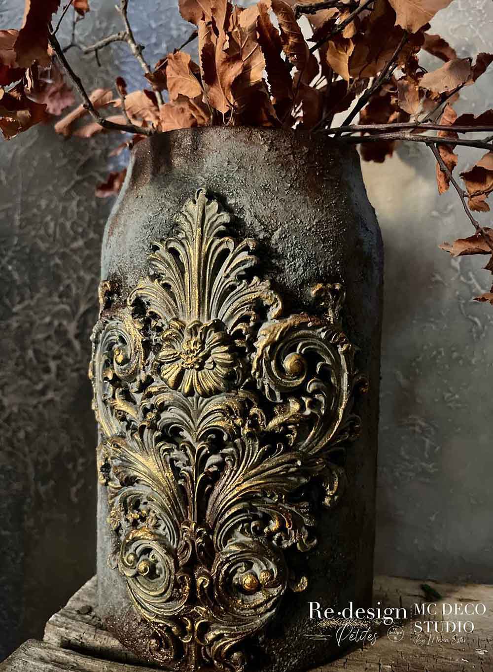 Salon De La Belle Epoque Decor Mould casting applied to a dark textured vase with ornate raised scrollwork, antique gold highlights, and dried leaves.