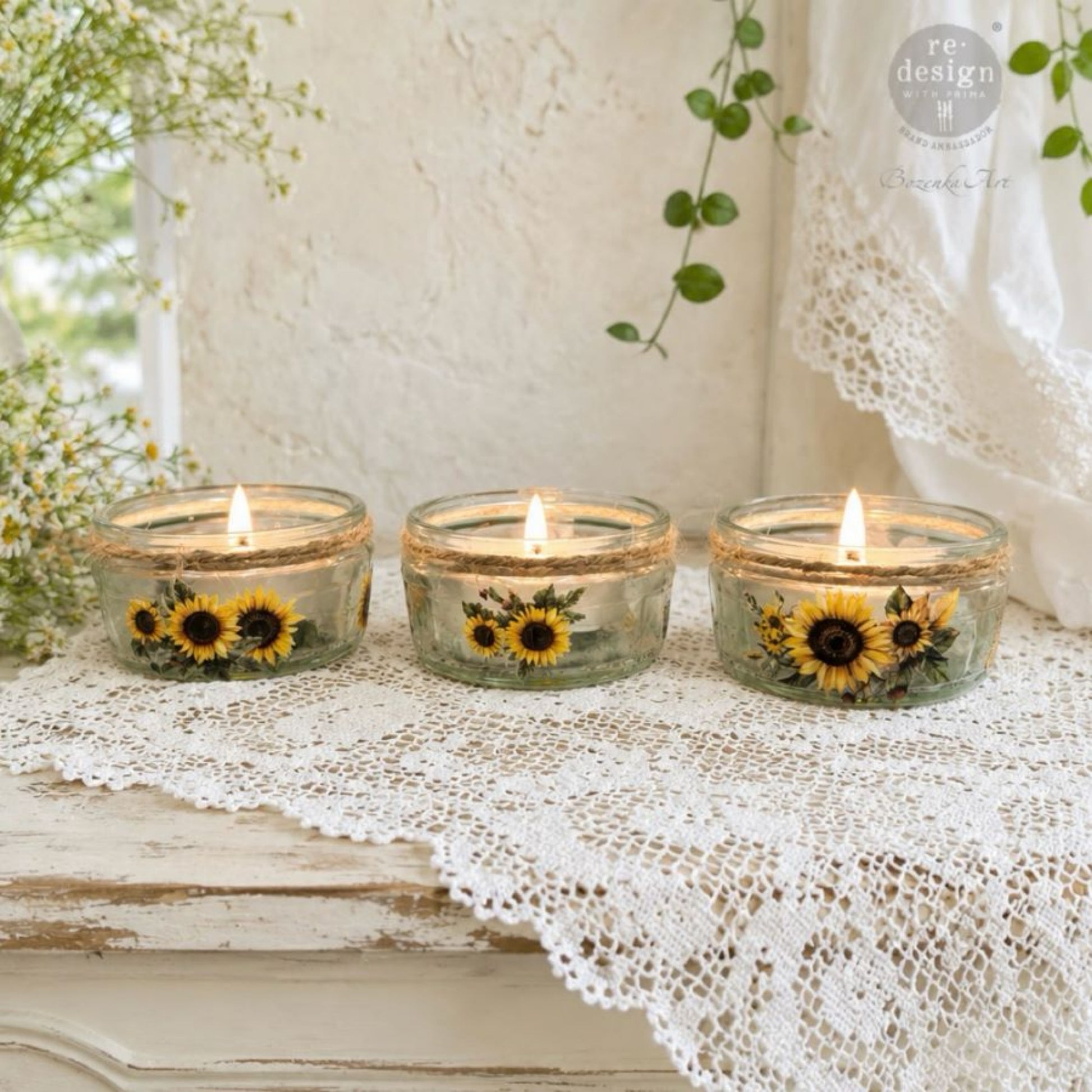 Three lit glass candle holders decorated with Sun-Drenched Harvest sunflower Luxe Transfers on a vintage lace-covered table.
