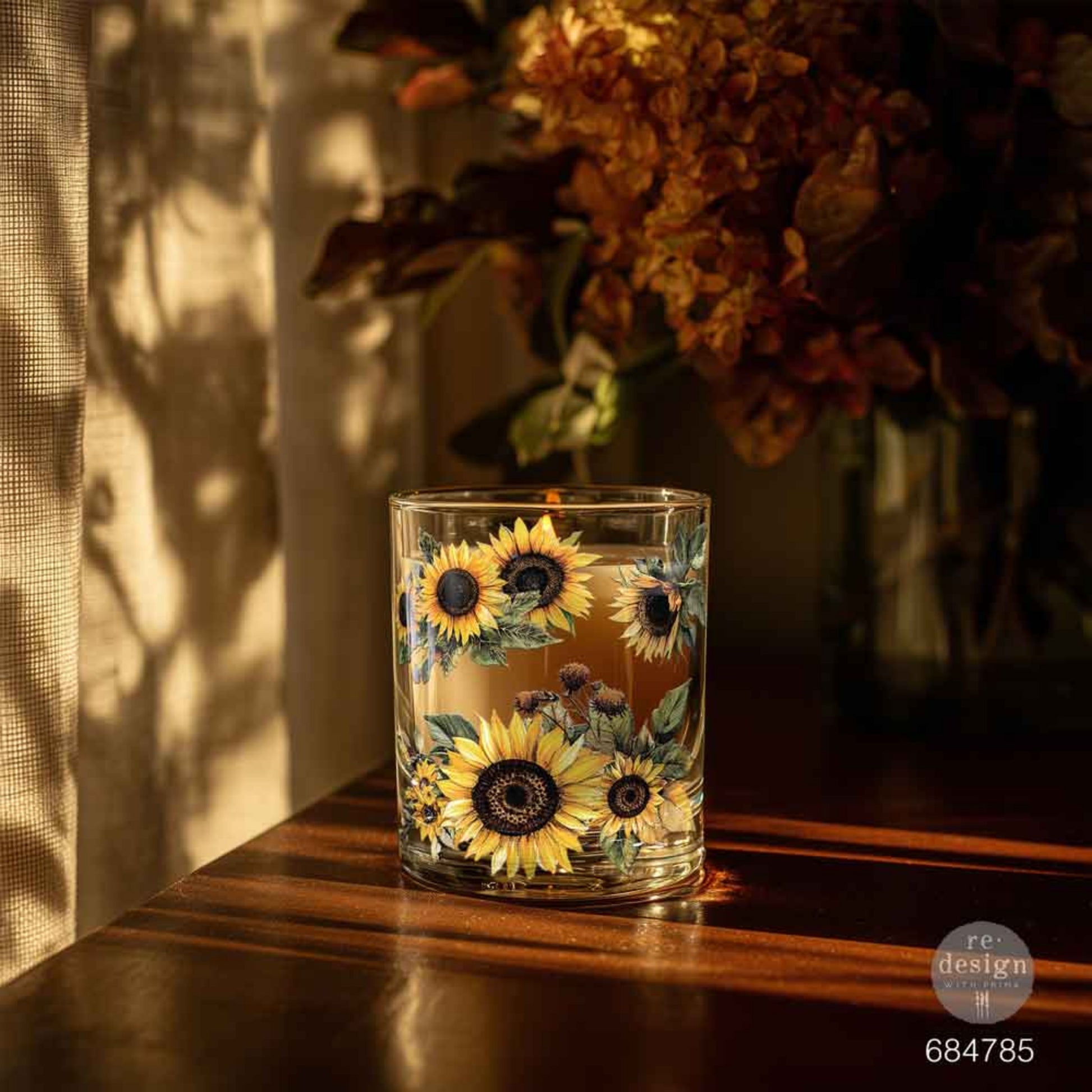 Clear glass candle holder decorated with sunflower and greenery Luxe Transfers in golden autumn light.
