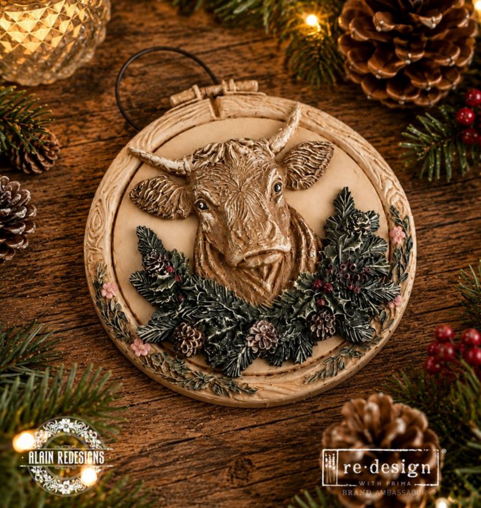 Round holiday plaque decorated with a Highland-style cow casting, evergreen branches, holly, berries, and pinecones.